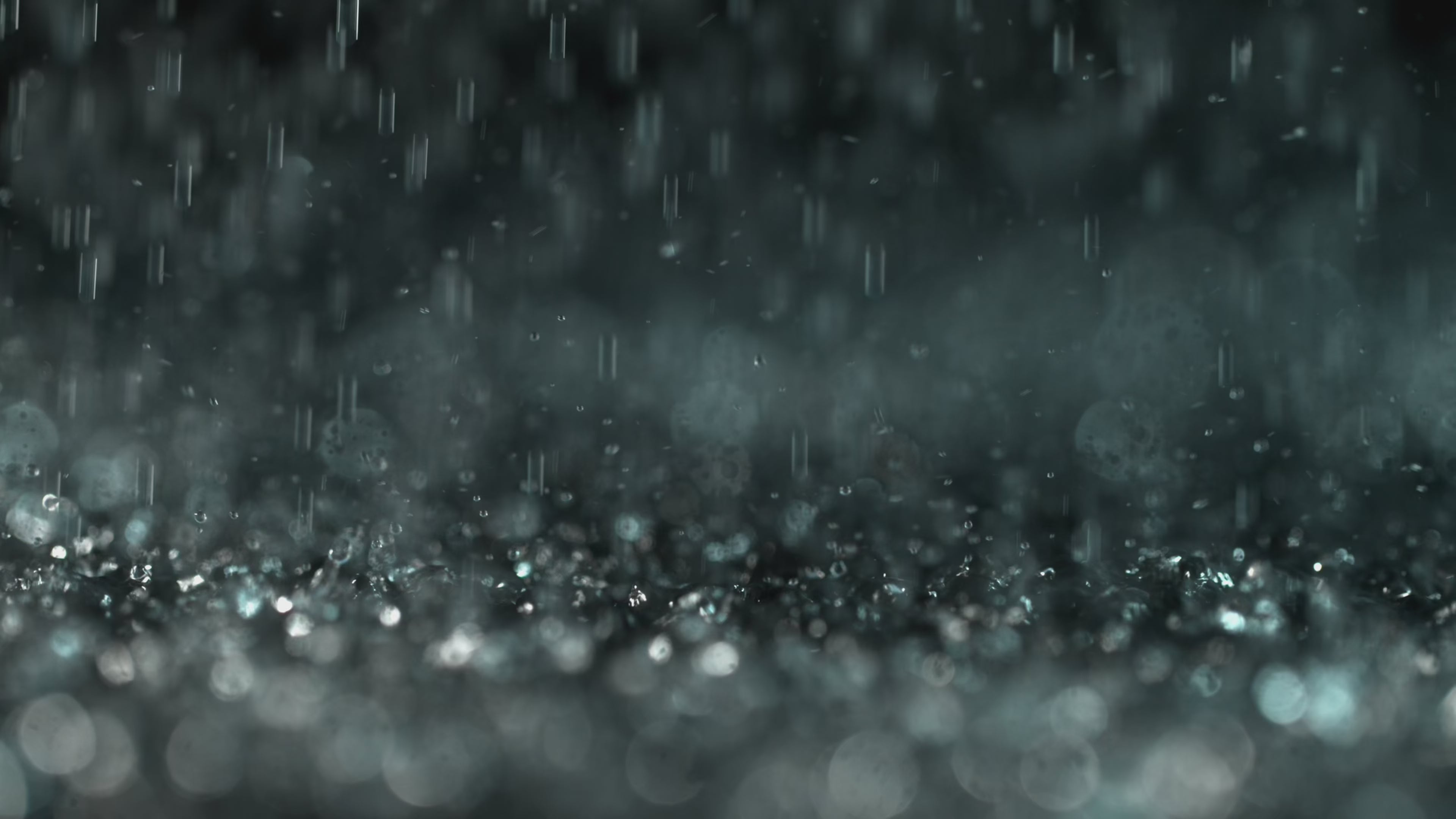 Load video: Close-up of soft rain falling in slow motion, with water droplets splashing gently on a dark surface — evoking calm, stillness, and deep relaxation.