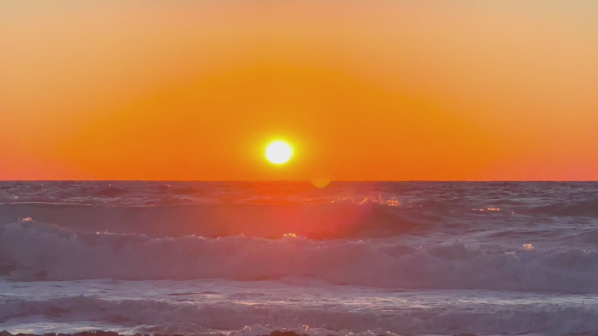 Załaduj wideo: Video of Golden sunset over ocean waves, gentle wave sounds as sunlight reflects gently on the sea&#39;s surface in a moment of calm and radiant stillness.